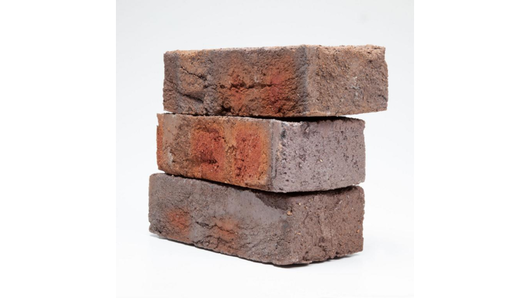 Drei übereinander gestapelte Fassadenziegel mit einer rustikalen, tief genarbter Oberfläche, in verschiedenen Brauntönen und Texturen.